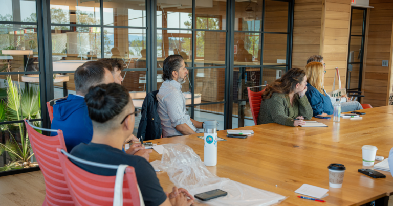 Small group of B2B marketers in a workshop session around a wooden conference table in a modern glass-walled venue at an Exit Five event