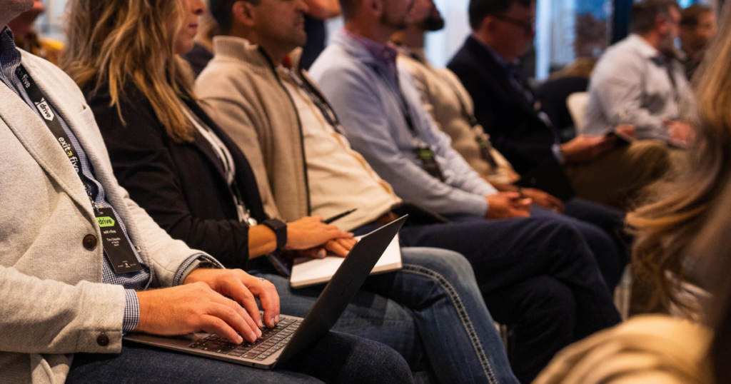Row of B2B marketing professionals wearing Exit Five lanyards with laptops open, actively engaged during a conference session