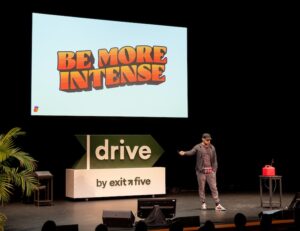 Louis Grenier on stage at Drive 2026 in front of a screen reading BE MORE INTENSE
